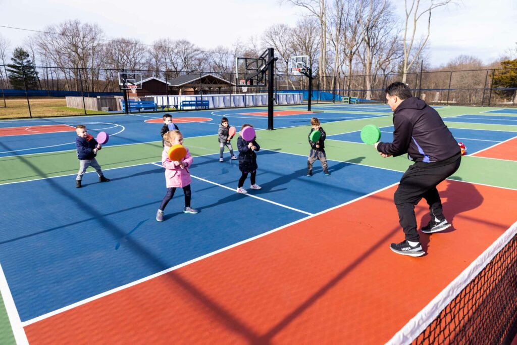 Kids being taught how to swing toy tennis rackets.